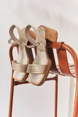 Sandalias de tacón color beige con puntera cuadrada, tiras doradas en el empeine y tobillo, y taco cuadrado.