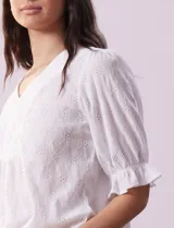 Blusa blanca calada con escote en V, mangas cortas con hombros fruncidos y puños elastizados.