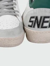 Championes Golden Goose modelo Ball Star, color blanco con detalles en gris y verde. Presentan una estrella plateada en el lateral, puntera y talón en gamuza gris, y detalle verde en el talón. Cordones grises y suela color crema con efecto envejecido.