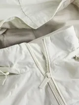 Campera blanca de poliéster con capucha y cierre frontal con cremallera. Tiene cuello alto, puños y ruedo elásticos, y un parche de goma con el logo de Calvin Klein en la manga izquierda.