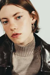 Par de aros pequeños plateados de metal con forma irregular y relieve, parecidos a una hoja o punta estilizada.