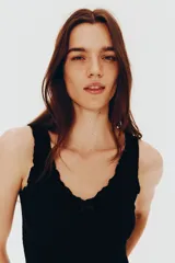 Top corto negro en punto suave con efecto arrugado, escote de pico con moño de satén y costura fruncida.