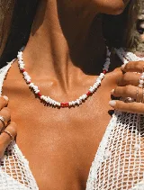 Collar corto con cuentas de piedra natural blanca y cristalitos facetados rojos. Cierre de acero con baño en oro.