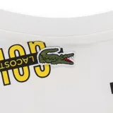 Camiseta blanca de Lacoste con estampado de la palabra 'GOLF' en amarillo y negro. Cuello redondo y manga corta.