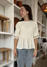 Blusa color crema con cuerpo delantero fruncido tipo smock y vuelo peplum a la altura de la cintura. Mangas globo 3/4 con volado en los puños.