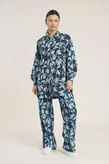 Conjunto de camisa de manga larga con botones y pantalón de corte recto, ambos con estampado de hojas y flores en tonos azul y naranja sobre fondo azul marino.