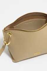 Bolso bandolera de piel vacuna negra, con forma trapezoidal y estructura rígida. Posee asa regulable, cierre de cremallera, bolsillo interior y charm decorativo con borlas en tonos tierra y dorado.