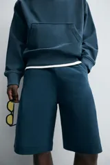 Bermuda azul petróleo de corte relaxed fit, confeccionada en algodón. Tiene cintura elástica ajustable con cordón, bolsillos laterales y un bolsillo trasero.