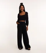 Pantalón de vestir negro, de corte recto, con bolsillos laterales y traseros. Se ajusta a la cintura con cinturón de cuero marrón.