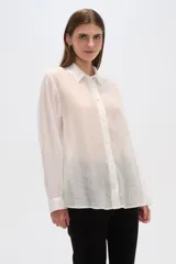 Camisa blanca traslúcida de lyocell, corte holgado, con cuello camisero, cierre frontal con botones y mangas largas con puños abotonados.