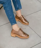Zapato acordonado color bronce de cuero vacuno con perforaciones decorativas, taco de madera con folia en cuero de 4cm y entre suela de goma de 1,5cm. Horma de punta redonda y cómoda.
