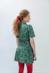 Vestido corto verde con estampado de flores negras, cuello camisero, mangas cortas abullonadas y falda con volantes.