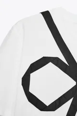 Camiseta blanca de corte recto, cuello redondo y mangas cortas. Presenta un lazo negro estampado en el frente.