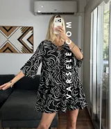 Vestido corto color verde oliva con estampado de hojas en blanco y negro, escote con lazo ajustable y mangas 3/4 acampanadas.