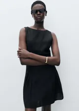 Vestido corto negro con cuello barco, sin mangas, corte evasé y detalle de pliegues en la falda.