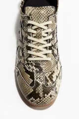 Zapatillas deportivas de perfil bajo con cordones blancos y suela de goma color caramelo. El cuerpo del calzado presenta un estampado de piel de serpiente en tonos beige, marrón y negro.