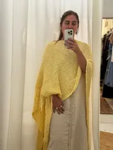 Ruana tejida a mano con hilo color amarillo claro, con flecos en el borde inferior.