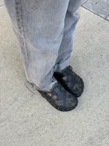 Zueco de cuero negro con hebilla ajustable, tachas doradas y bordado artesanal.