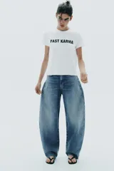 Camiseta blanca de algodón con cuello redondo, manga corta y texto 'FAST KARMA' estampado en el frente.