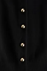 Saco de punto negro con cuello redondo y botones dorados. Tiene remate acanalado en cuello, puños y bajo.