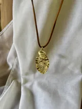 Collar con cordón doble marrón y dije dorado con forma de hoja con perforaciones.