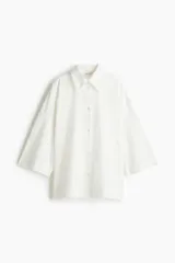 Camisa blanca de corte amplio con cuello clásico, cierre frontal con botones y mangas tres cuartos.