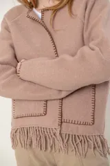 Chaqueta corta color gris oscuro confeccionada en lana merino hervida, con cuello redondo, mangas largas y bolsillos frontales. Presenta detalle de flecos en el ruedo.