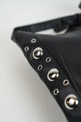 Cartera bandolera negra de cuero sintético con flecos en la parte inferior y detalles de ojalillos metálicos en los laterales.