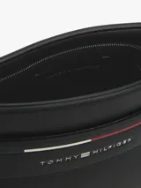 Bandolera negra de Tommy Hilfiger con acabado texturizado, cierre de cremallera, correa ajustable, compartimento principal, bolsillo interior con cremallera, logo metálico de Tommy Hilfiger en la parte delantera y detalles distintivos de la marca.