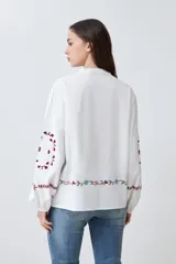 Camisa blanca con bordados florales en tonos rosa, azul y verde.