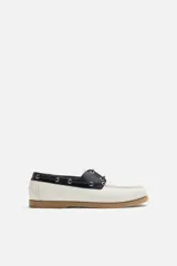 Zapato náutico de cuero blanco con detalles en negro y suela marrón.