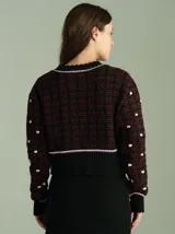 Cardigan de punto color borgoña con diseño geométrico en blanco y detalles en azul. Tiene cuello redondo, cierre frontal con botones rojos y mangas largas con puños acanalados.