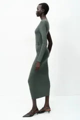 Vestido midi negro de punto, con cuello asimétrico, manga sisa, aplique metálico dorado en el hombro y drapeado lateral.