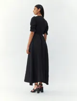 Vestido negro de corte midi, con escote en V cruzado, mangas 3/4 con elástico en los puños y lazo en la cintura.