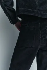 Pantalón ancho de pana color negro, de tiro medio, con trabillas en la cintura, bolsillos delanteros y cierre frontal con cremallera, botón y gancho metálico.