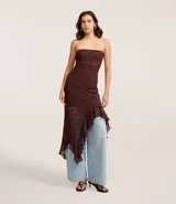 Vestido blanco sin breteles, confeccionado en encaje floral. Presenta un escote recto y un bajo asimétrico con volados.