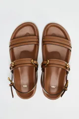 Sandalias planas color marrón con doble tira delantera con detalle de hebilla y cierre mediante hebilla en la pulsera al tobillo.