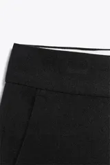 Pantalón negro tobillero de tiro alto con bolsillos delanteros y traseros. Tiene abertura lateral en el bajo y cierre frontal con cremallera y botón.