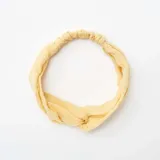 Diadema de gasa de algodón color amarillo claro con nudo frontal y elástico en la parte posterior.