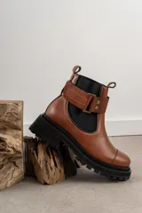 Botas de cuero color marrón oscuro, estilo Chelsea, con elástico lateral negro y suela track negra. Incluye correa de cuero desmontable con hebilla.