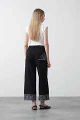 Pantalón de denim azul oscuro con bordado estilo bandana en blanco en los laterales de las piernas y en los puños. El corte es recto y amplio, llegando al tobillo.