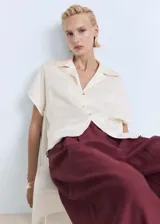 Camisa color crema de manga corta con tejido satinado, corte regular, cuello camisero y cierre delantero con botones.