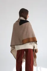 Ruana tejida con diseño geométrico en bloques de color beige, azul y naranja, con flecos en el borde inferior.