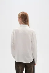 Camisa blanca de viscosa con cuello clásico, cierre frontal con botones y mangas largas. Presenta un sutil diseño de líneas verticales con strass. Corte al cuerpo.