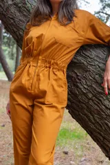 Mono color ocre de gabardina 100% algodón, con corte clásico, cierre frontal completo, pantalón largo con bolsillos, manga corta y cintura fruncida en la espalda.