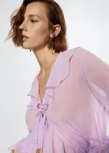 Vestido largo lila semitransparente con cuello en V, volantes en el escote y mangas largas con volantes.