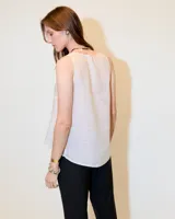 Top sin mangas blanco de lino, con escote redondo, corte en A, ruedo asimétrico y recortes laterales.