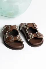 Sandalia tipo mule negra de cuero, con dos tiras ajustables con hebillas metálicas plateadas y apliques de tachas esféricas plateadas. Presenta un borde festoneado en la tira superior y suela de plataforma negra.