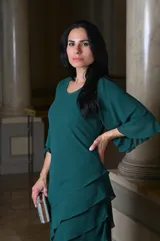Vestido largo de fiesta color verde oscuro, con mangas acampanadas y falda con volados en cascada. Incluye clutch plateado.