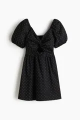 Vestido corto negro con lunares blancos, escote en V pronunciado, sección cut-out con detalle girado en el busto, espalda escotada fruncida, cierre oculto en un lateral y manga abullonada al codo con elástico fino en los puños.